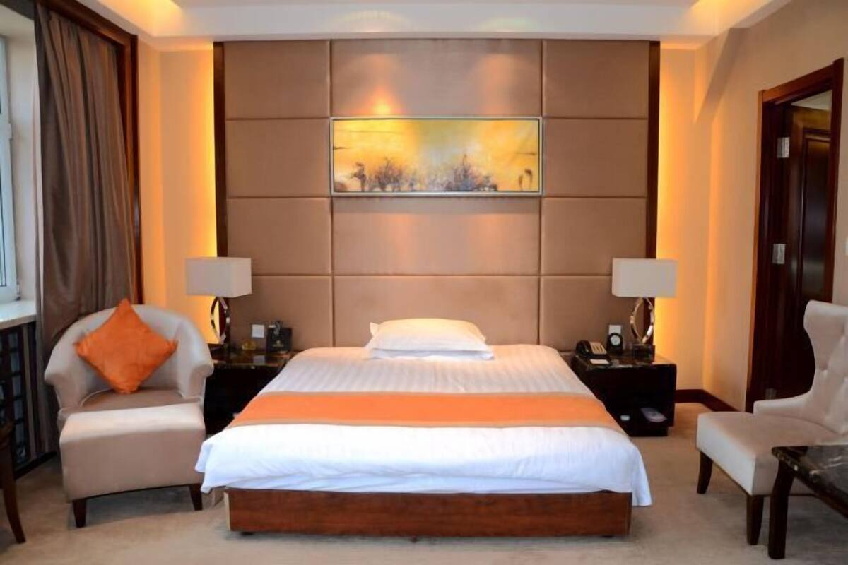 A hotel room with a large bed, two nightstands, a chair, a desk, and a painting on the wall.