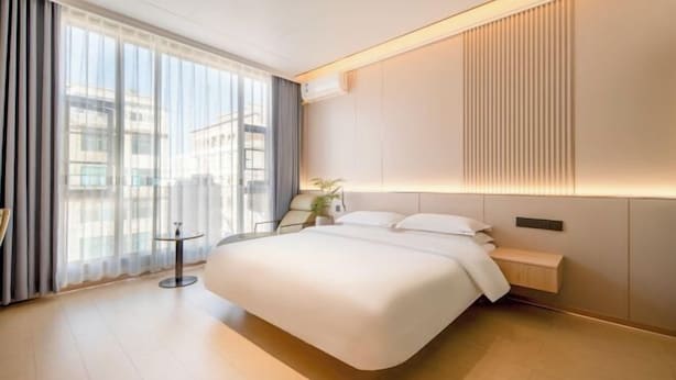 A modern hotel room with a large bed, a bedside table, a small round table, and a view of the city through large windows. - Qujing 1 +1 Express Hotel (Qujing)