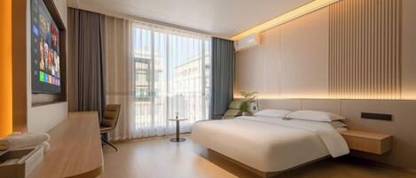 A modern hotel room with a large bed, a desk, a chair, and a TV mounted on the wall.