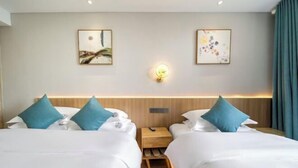 Ein Hotelzimmer mit zwei Betten, jeweils mit weißer Bettwäsche und türkisfarbenen Kissen, einem hölzernen Nachttisch und einer wandmontierten Lampe.