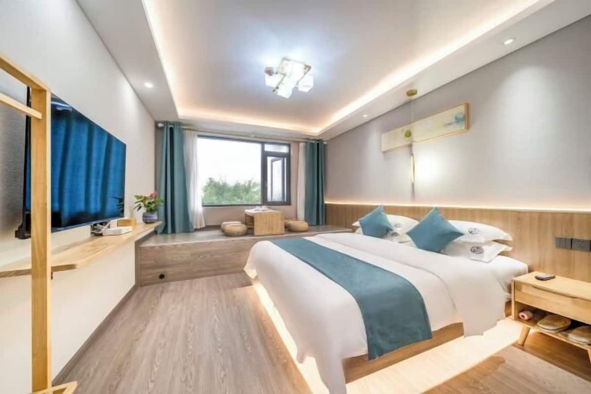 A modern hotel room with a large bed, a bedside table, a TV, and a window with curtains.