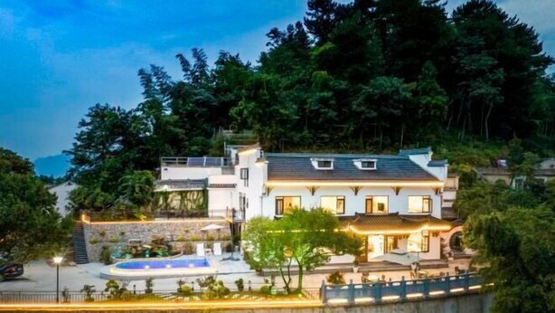Ein mehrgeschossiges Haus mit Schwimmbad, umgeben von üppiger Vegetation und einer steilen Böschung.