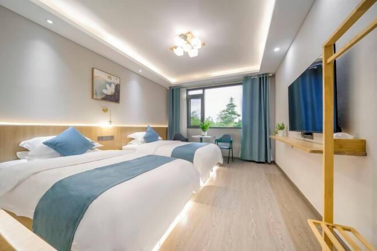 A hotel room with two beds, a small table, a TV, and a window with curtains.