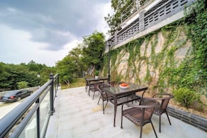 An outdoor patio with a table and chairs, a railing, and a view of a road and greenery.
