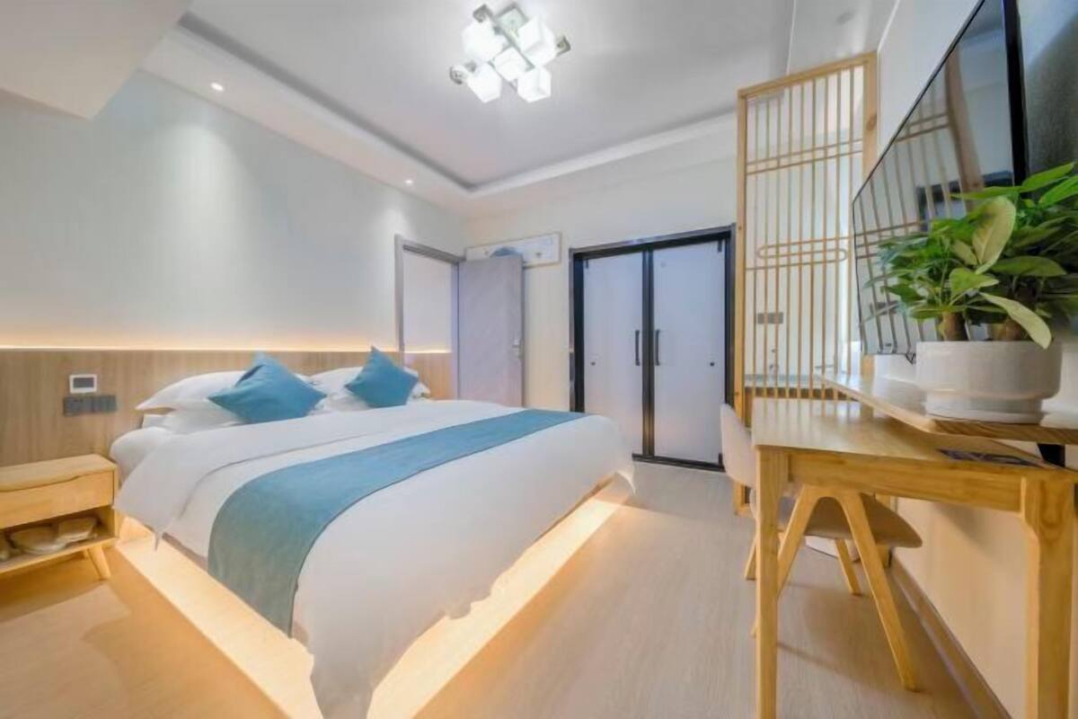 A modern bedroom with a large bed, bedside tables, a wooden desk, and a potted plant.