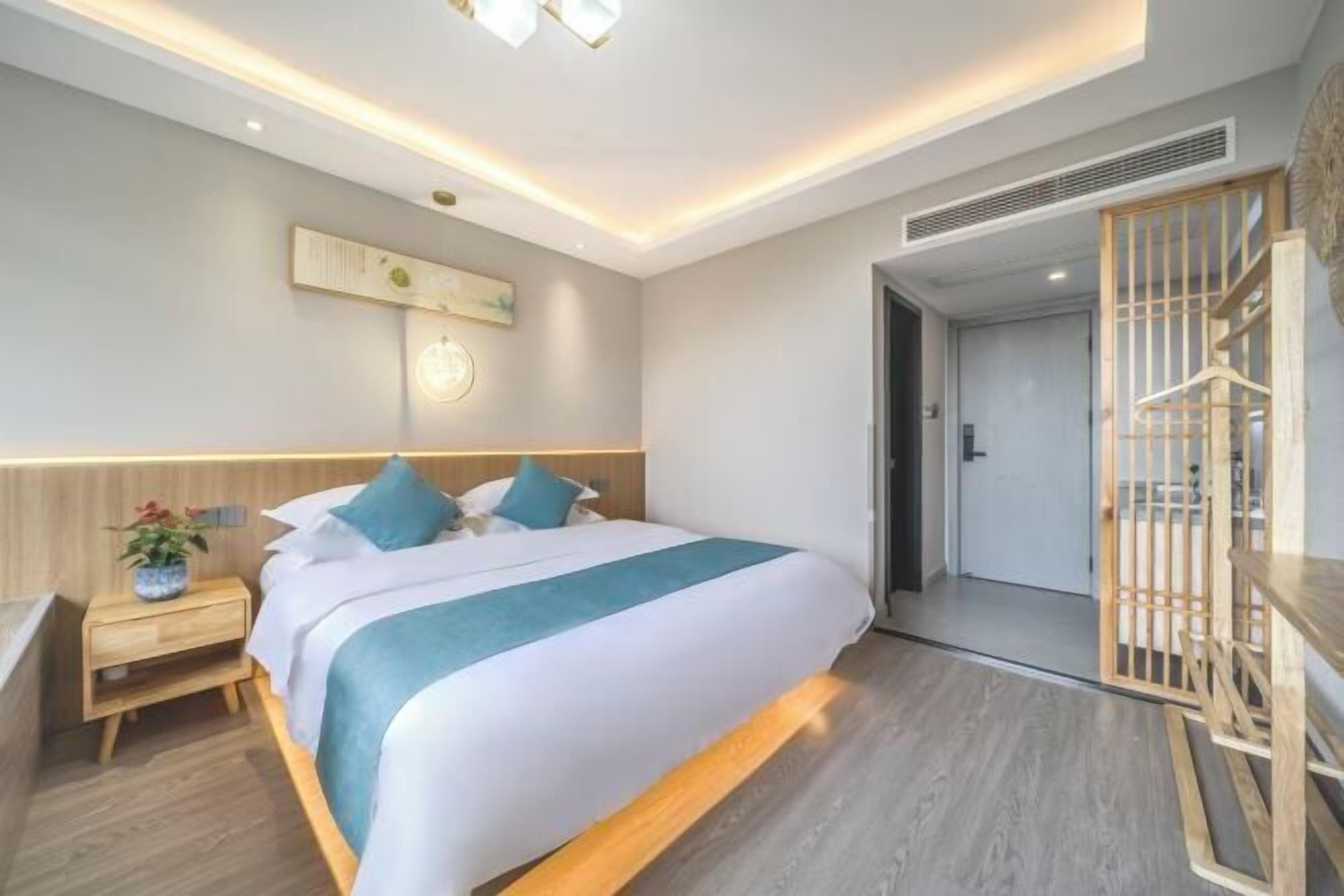 Una habitación de hotel moderna con una cama grande, mesita de noche y vistas al pasillo.