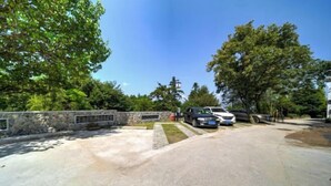 Ein gepflasterter Weg führt zu einem Gebäude, an dessen Seite eine Steinmauer und auf der anderen Seite Bäume stehen.