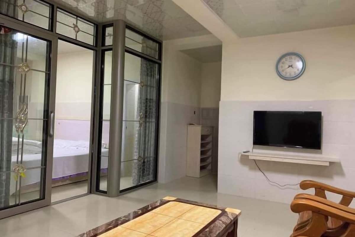 Quarto com cama, televisão fixada na parede e uma cadeira de madeira.