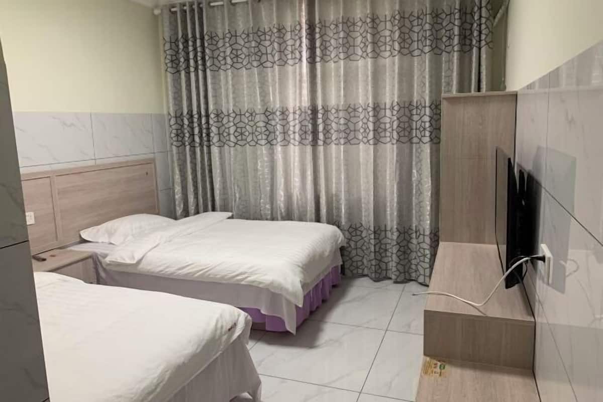 Quarto de hotel com duas camas, televisão, guarda-roupa e cortina de chuveiro com padrão geométrico.