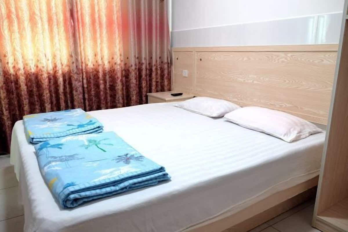 Uma cama de solteiro com cabeceira de madeira, mesa de cabeceira e um cobertor azul dobrado com padrão floral.