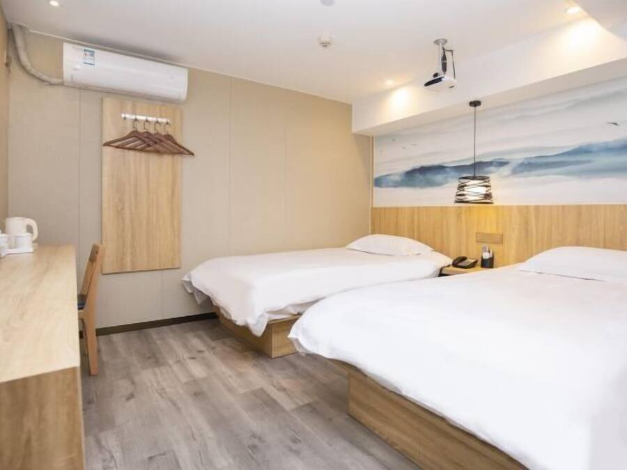 Habitación de hotel con dos camas, un escritorio de madera, aire acondicionado de pared y un cuadro de un cielo nublado.