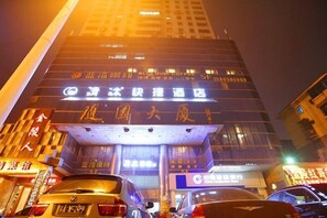 A hotel with illuminated signage in a foreign language, multiple floors, and a busy street with parked cars. - Qingmu Hotel (Nanjing Wutaishan Guangzhou Road Suiyuan Building) (Nanjing)