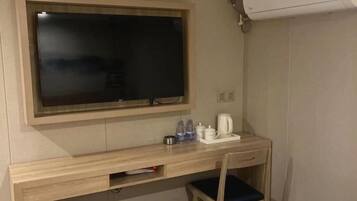 A room with a TV mounted on the wall, a wooden desk with a chair, and a coffee maker on the desk.