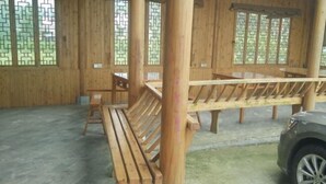 Un intérieur en bois avec des bancs et des tables, de grandes fenêtres avec des vitraux décoratifs, et une voiture garée à l’extérieur.