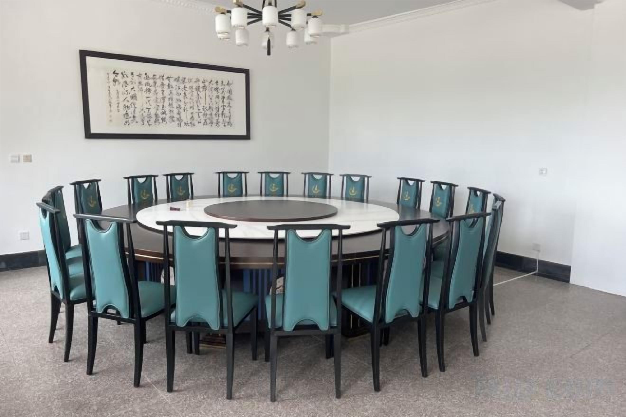 A conference room with a round table and chairs, a framed artwork on the wall, and a chandelier.