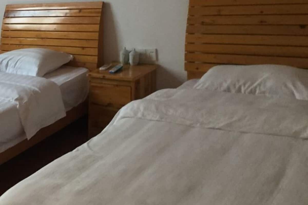Ein Zimmer mit zwei Betten, Holz-Kopfteilen, einem Nachttisch mit Fernbedienung und einer wandmontierten Leuchte.