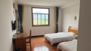 Une chambre avec deux lits, un bureau en bois, une chaise, une fenêtre avec des rideaux et une vue sur l’extérieur.