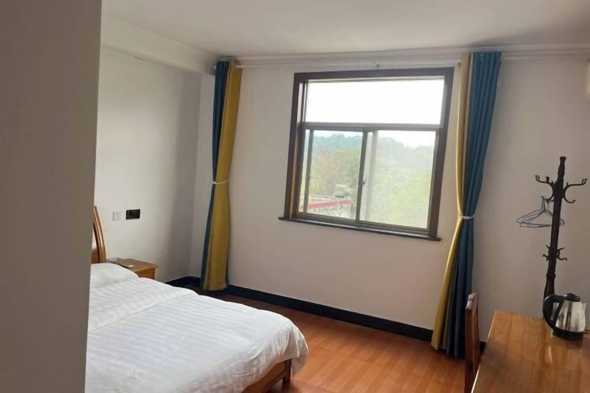 Ein Schlafzimmer mit einem Bett, einem Fenster mit Vorhängen, einem Kleiderständer und einem Holztisch.