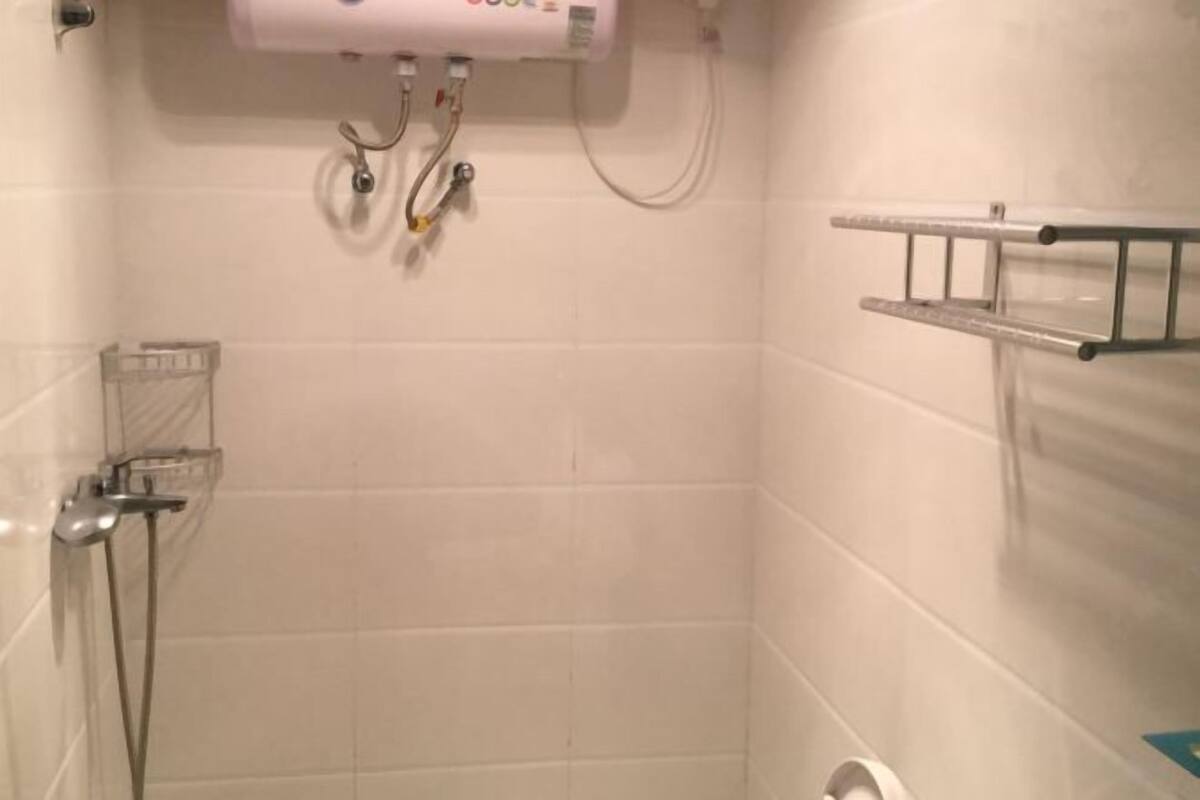 Ein Badezimmer mit weißen Fliesen, einer Dusche, einem Handtuchhalter und einer Toilette.