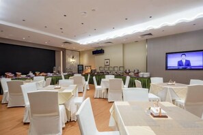 A conference room with round tables and chairs, a television screen, and a stage with a podium. - Landmark International Hotel(East Railway Station Tianhe Sport Center Branch) (Guangzhou)