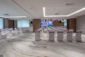 Un salón de conferencias con filas de sillas blancas, una pantalla grande al frente y un diseño moderno de techo.