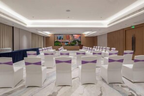 A conference room with rows of chairs, a stage, and a view of a cityscape through a large window. - Landmark International Hotel(East Railway Station Tianhe Sport Center Branch) (Guangzhou)