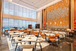 Un vaste espace dédié à la salle à manger, avec des tables et des chaises, de grandes fenêtres et un mur décoratif.