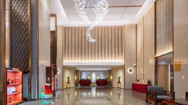 Un hall d’entrée moderne avec un sol réfléchissant, un luminaire au plafond original et un comptoir d’accueil.