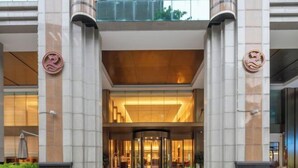 L’entrée d’un hôtel avec une porte tournante, de grandes colonnes et un balcon en verre.