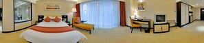 Quarto de hotel com cama grande, escrivaninha, televisão e espelho.
