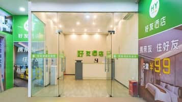 Zona de recepción de un hotel con puerta de vidrio, mostrador de recepción y pared verde con señalización.