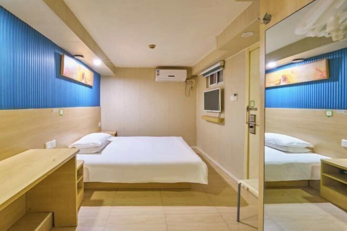 A hotel room with a bed, a desk, a mirror, a TV, and an air conditioning unit.