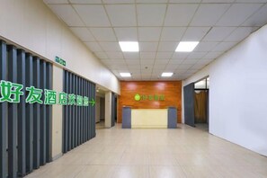 A hotel reception area with a reception desk, a wooden wall with a logo, and a corridor with a door on the right.