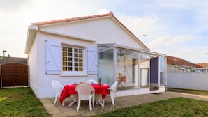 Une maison avec une véranda fermée par des baies vitrées, des murs extérieurs blancs et une nappe rouge.