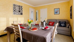 Un coin repas avec une table dressée pour quatre personnes, un vase de tulipes, une bouteille de champagne et une assiette de tomates.