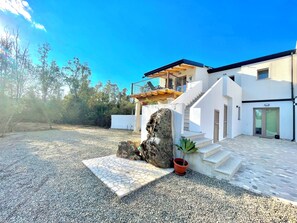 A modern house with a stone patio, a staircase, and a balcony.
