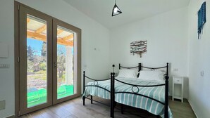 A bedroom with a bed, a nightstand, a wall-mounted artwork, and a sliding glass door leading to an outdoor area. - Le Corti Sarde Beach Deluxe (Bari Sardo)