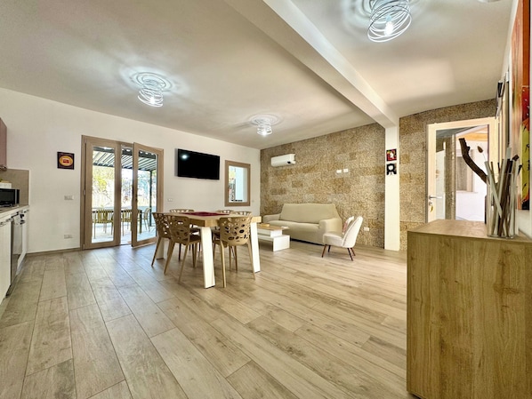 A modern living room with a sofa, dining table, and chairs, a flat-screen TV, and a stone accent wall.