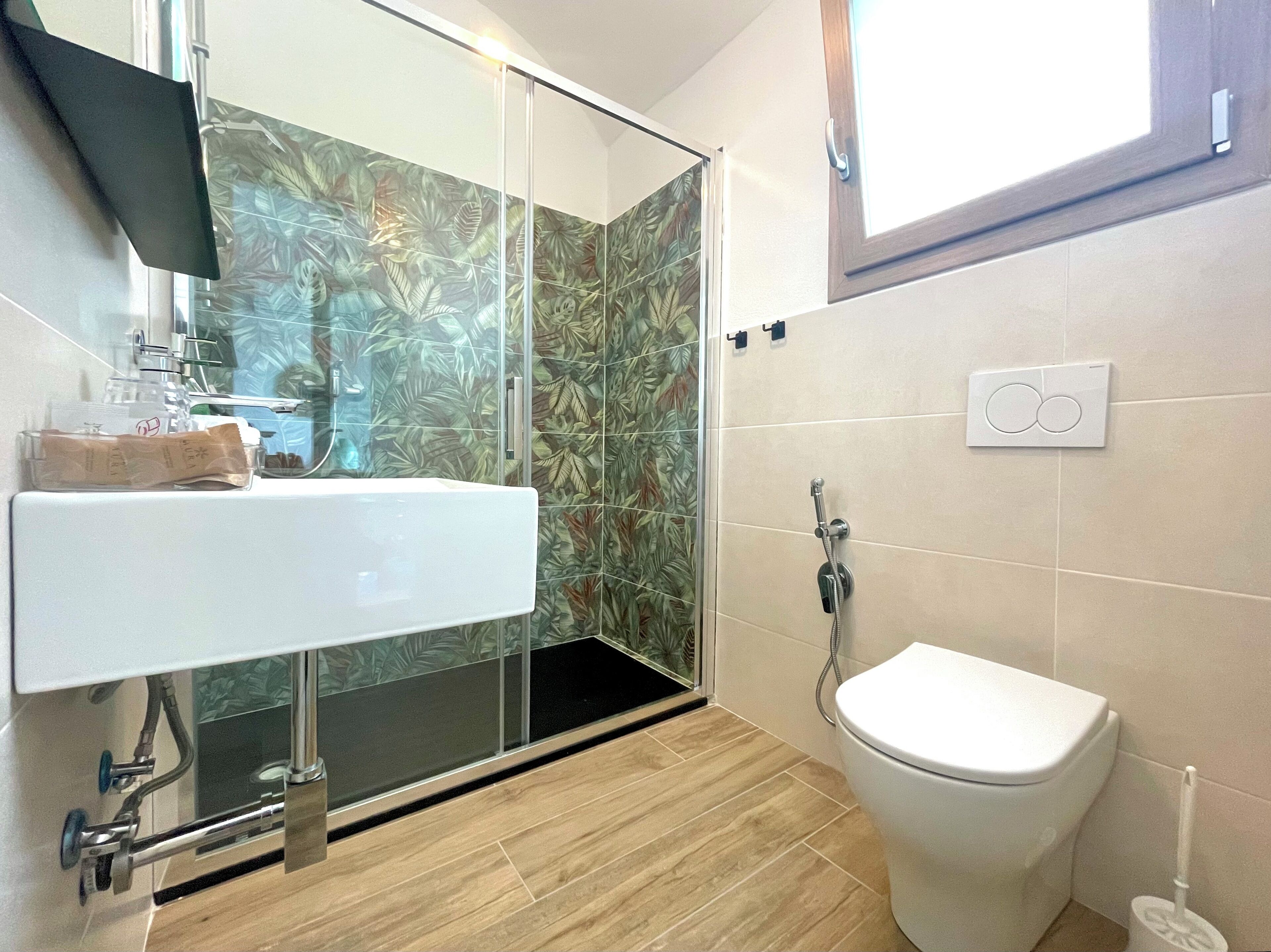 A bathroom with a shower, toilet, sink, and a window.