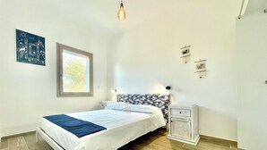 A bedroom with a bed, bedside tables, a window, and a wall-mounted light fixture. - "Le Corti Sarde Beach Apartments" (Bari Sardo)