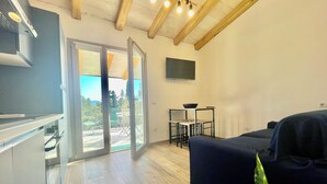 A modern living room with a dark blue sofa, a small table with a bowl, and a sliding glass door leading to an outdoor patio. - "Le Corti Sarde Beach Apartments" (Bari Sardo)