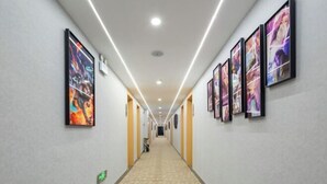 Un couloir d’hôtel avec des œuvres d’art encadrées accrochées aux murs, une moquette à motifs et un long couloir menant à une porte au bout.