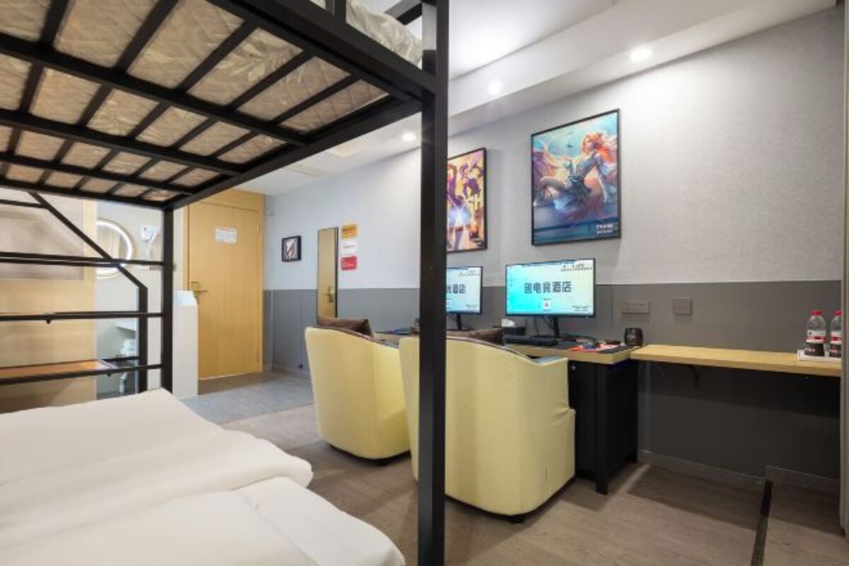 Une chambre d’hôtel avec un lit superposé, un bureau équipé de deux écrans et un coin salon avec des fauteuils.