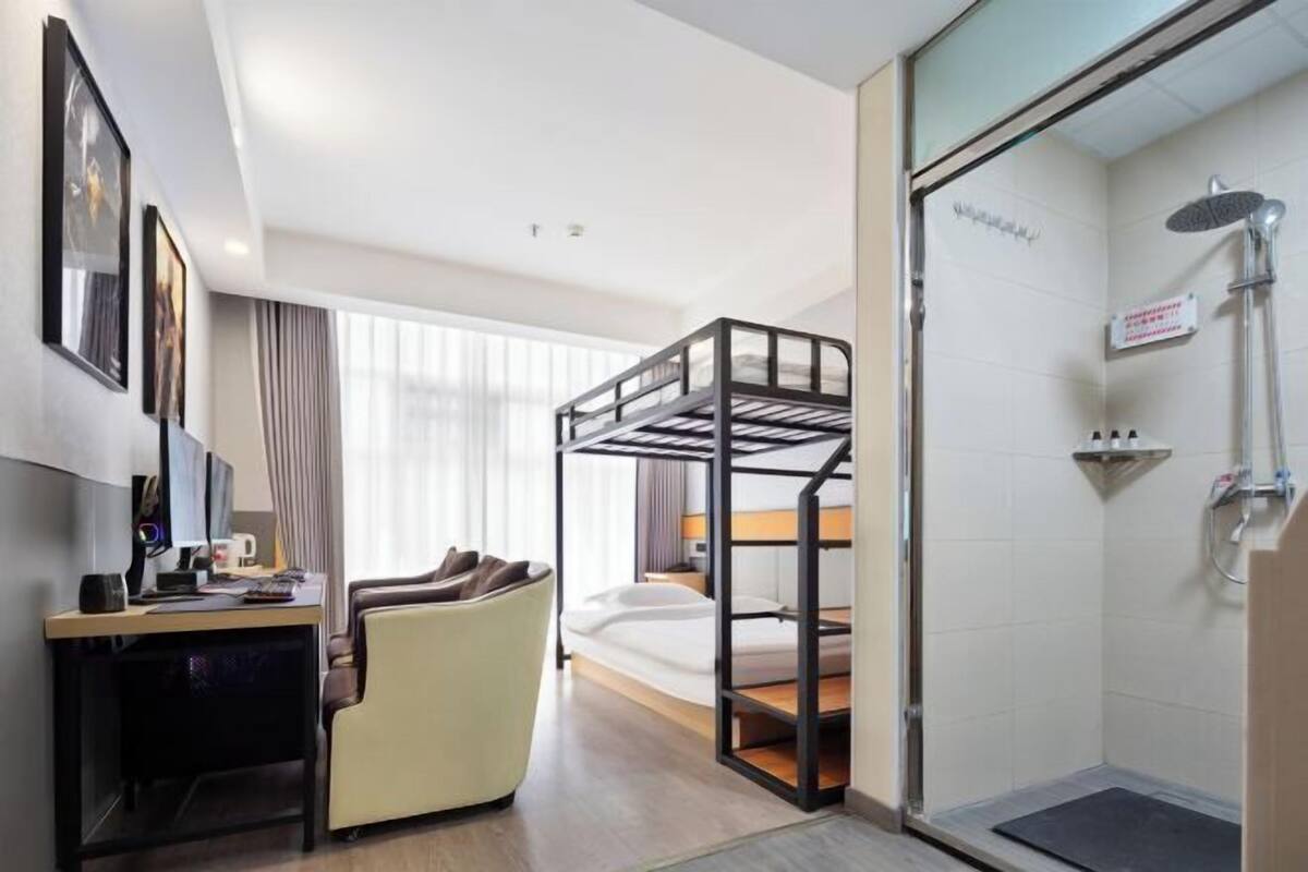 Ein Hotelzimmer mit Etagenbett, Schreibtisch mit Computer, Stuhl, Dusche und einem Bett.