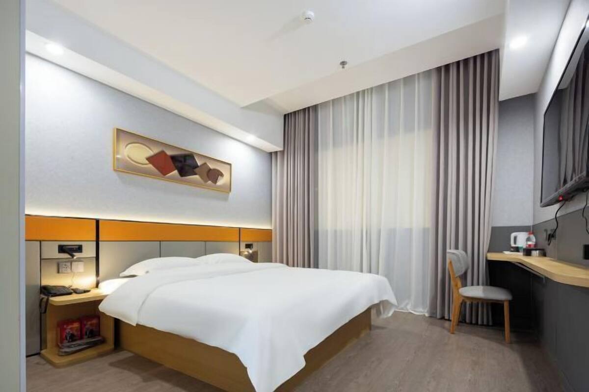 Ein Hotelzimmer mit Bett, Nachttisch, Lampe, Stuhl, Schreibtisch und Vorhängen.