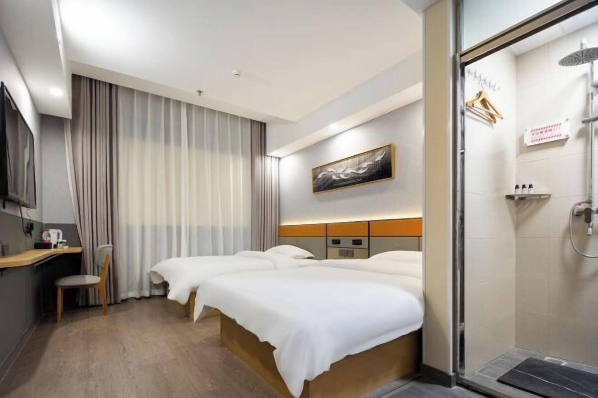 Ein Hotelzimmer mit Bett, Sessel, Schreibtisch, Dusche und einem Bild an der Wand.