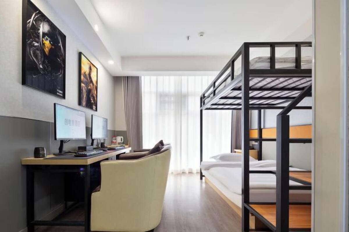 Ein Hotelzimmer mit einem Etagenbett, einem Schreibtisch mit Computer, einem Stuhl und zwei Bildern an der Wand.