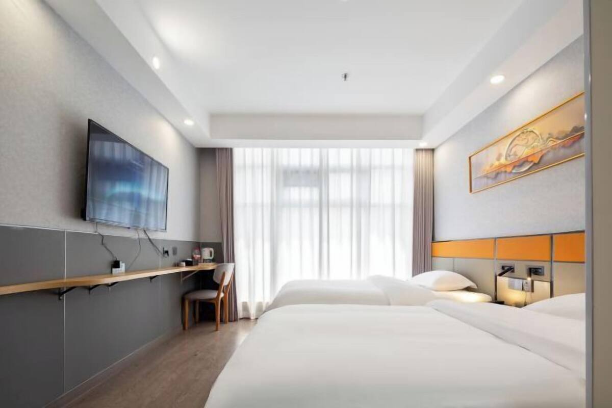 Ein Hotelzimmer mit Bett, Schreibtisch, Stuhl, Fernseher und einem Fenster mit Vorhängen.