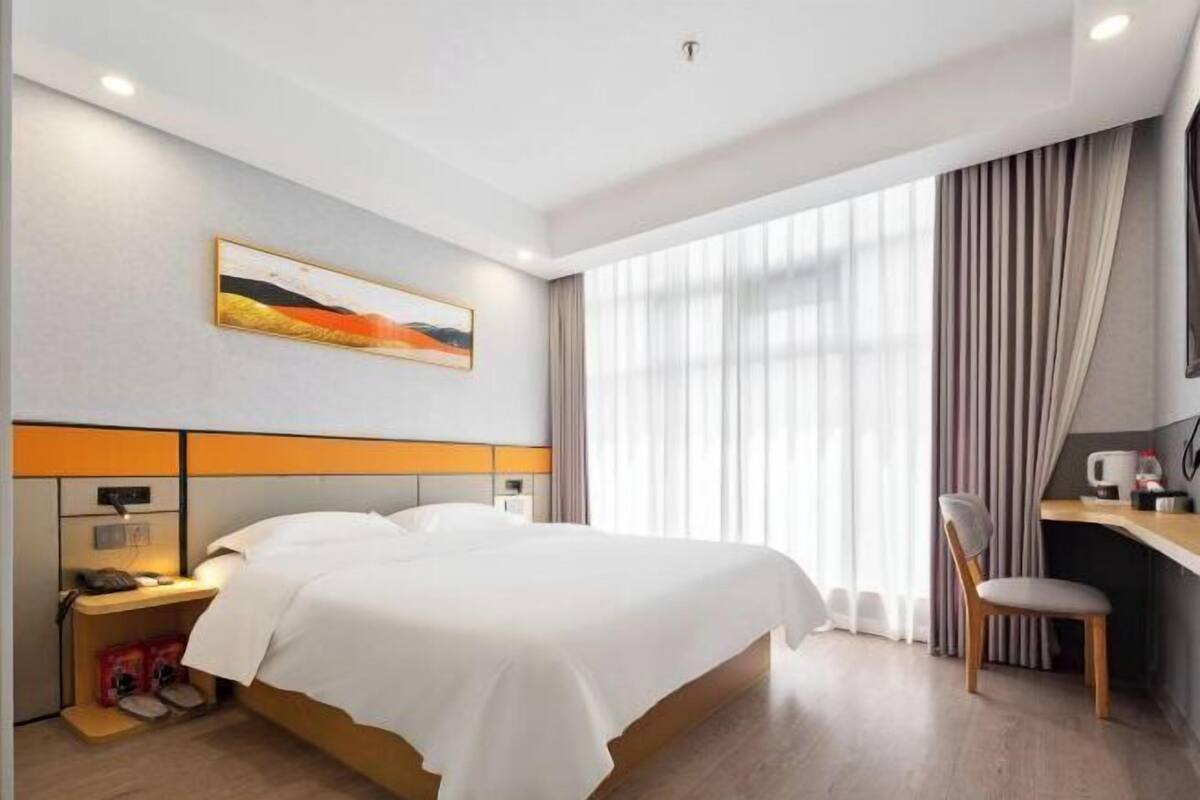Ein Hotelzimmer mit Bett, Schreibtisch, Stuhl, einem Bild an der Wand und einem Fenster mit Vorhängen.