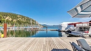 Une jetée en bois avec un bateau, un espace abrité doté d’un auvent à rayures et un paysage montagneux en arrière-plan.